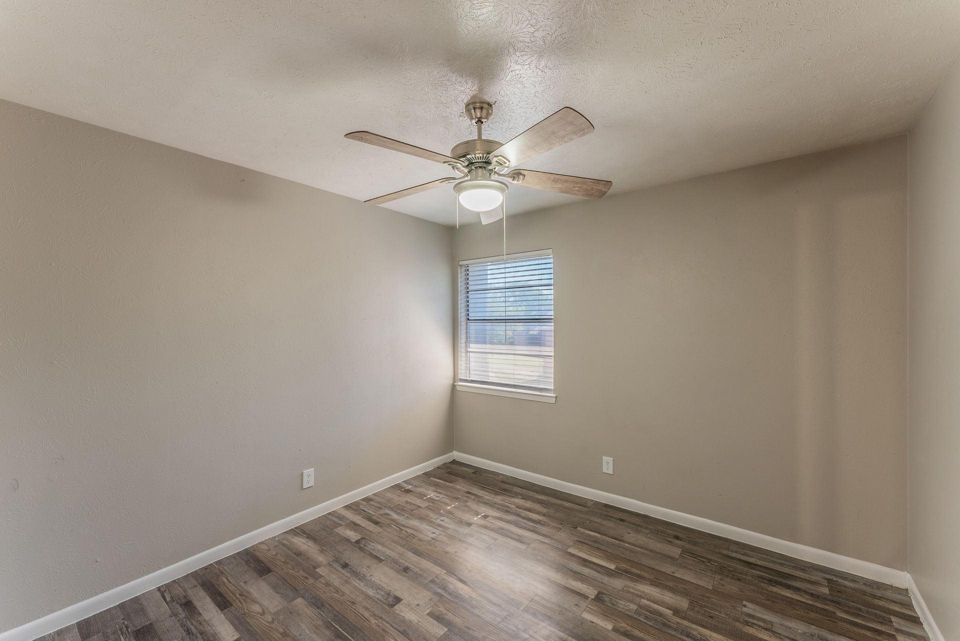 An empty bedroom with a ceiling fan and a window.