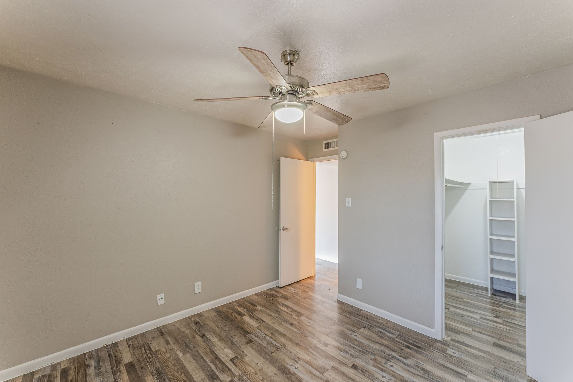 An empty bedroom with hardwood floors and a ceiling fan.