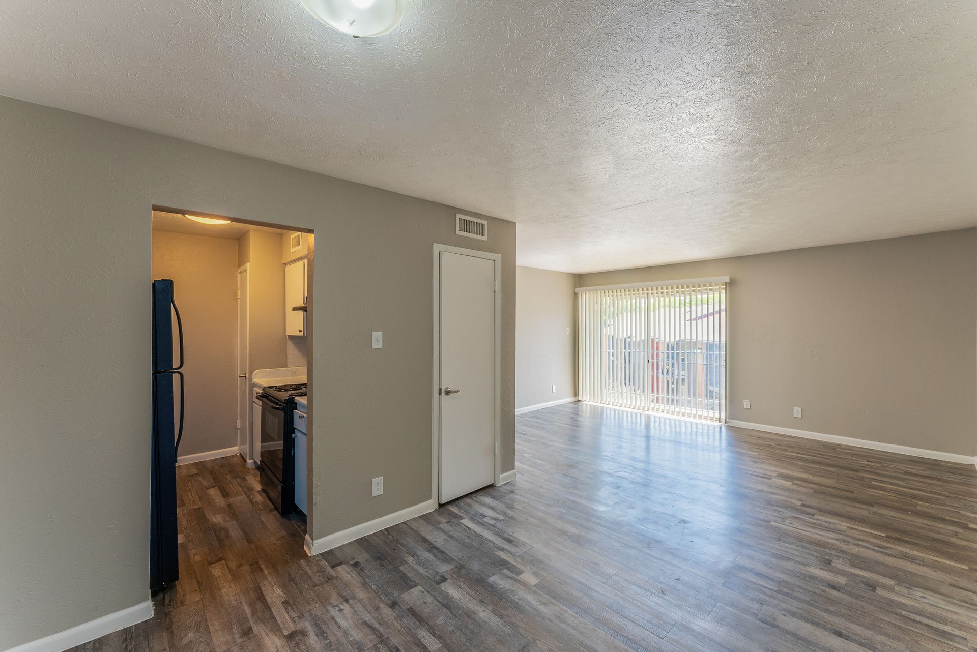 A living room with hardwood floors and a sliding glass door leading to a kitchen.