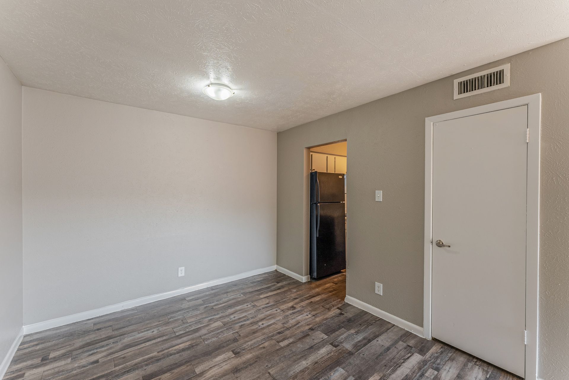 An empty living room with hardwood floors and a refrigerator.