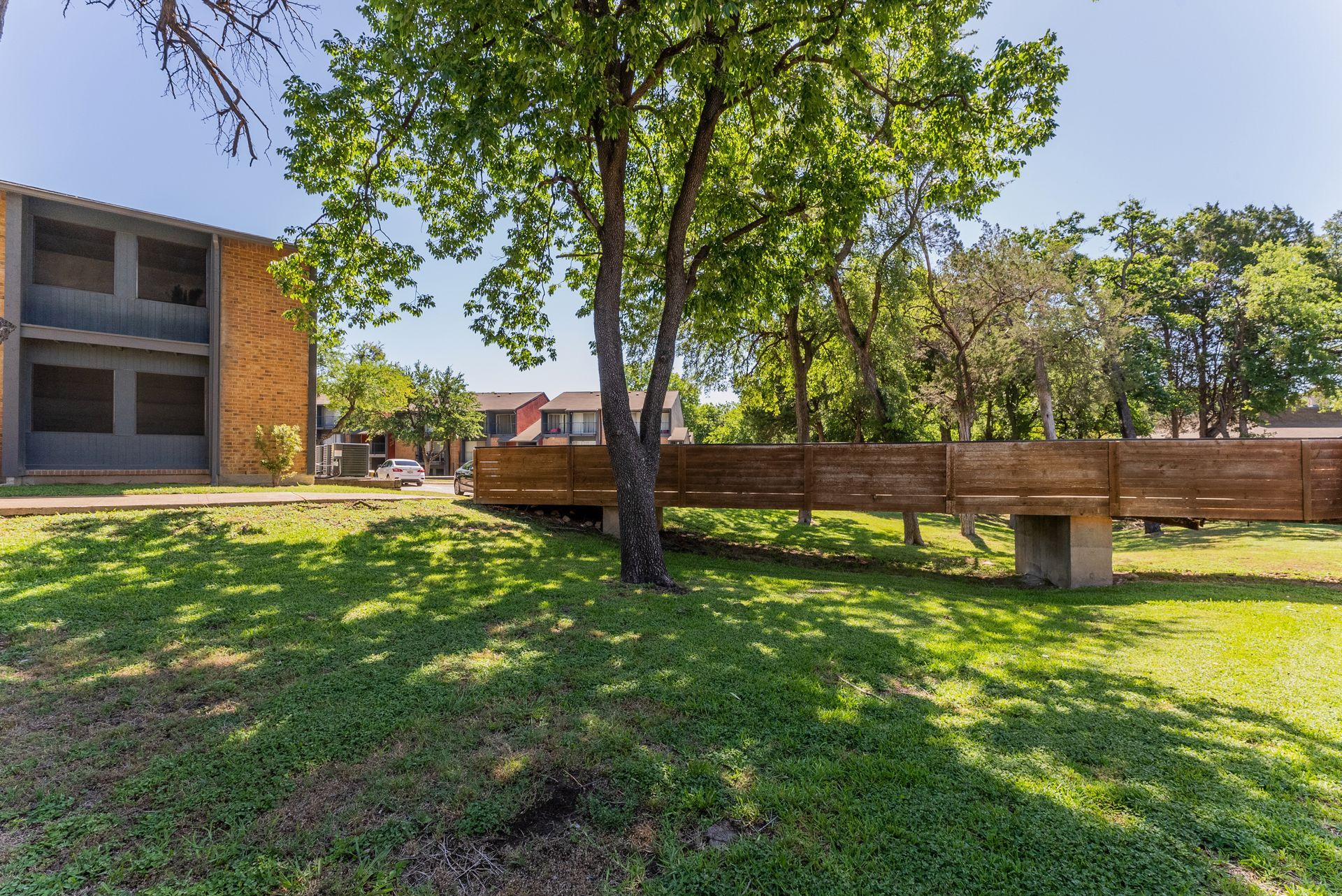 A wooden bridge is going over a grassy field in front of a building.