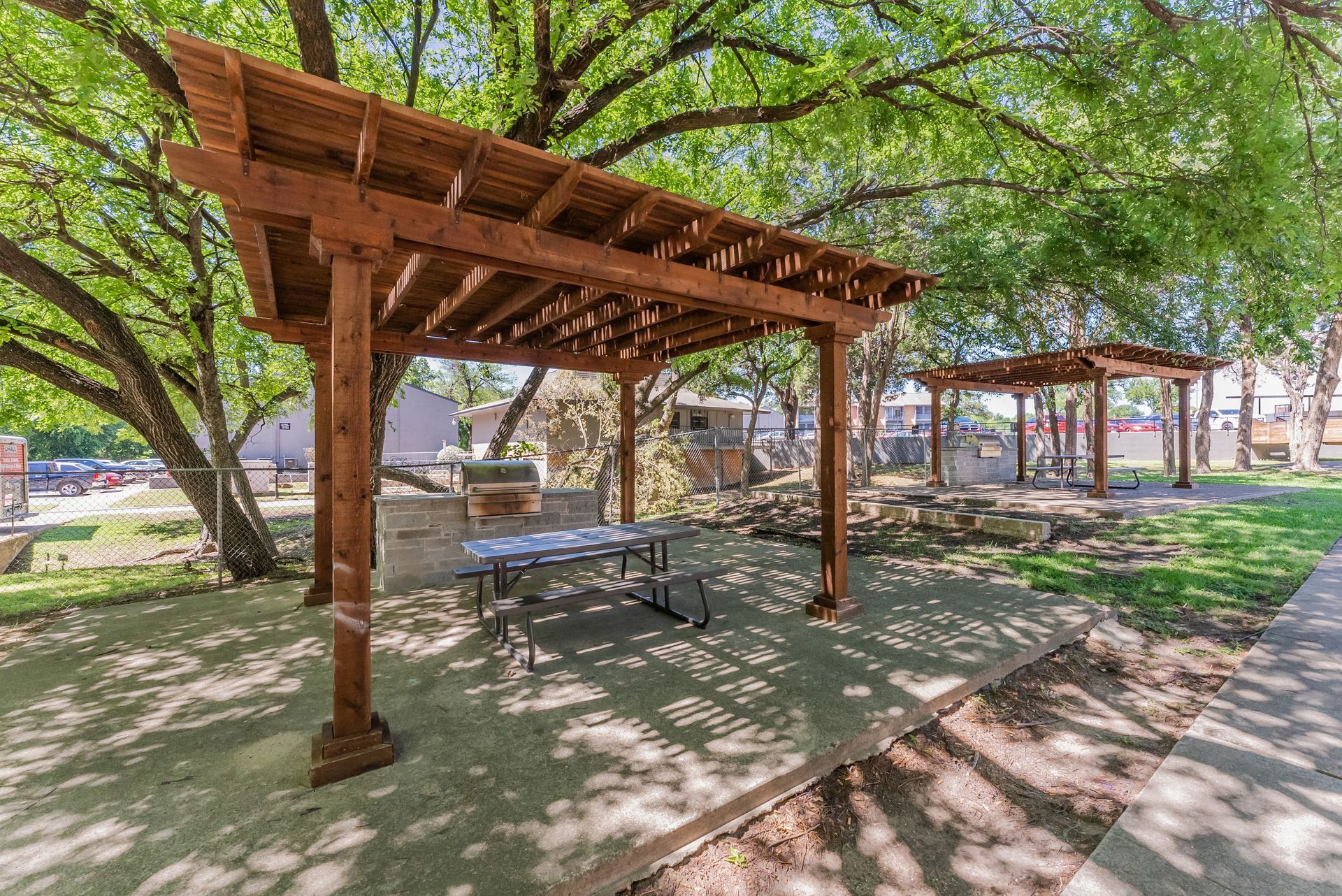 A wooden pergola with a picnic table underneath it in a park.