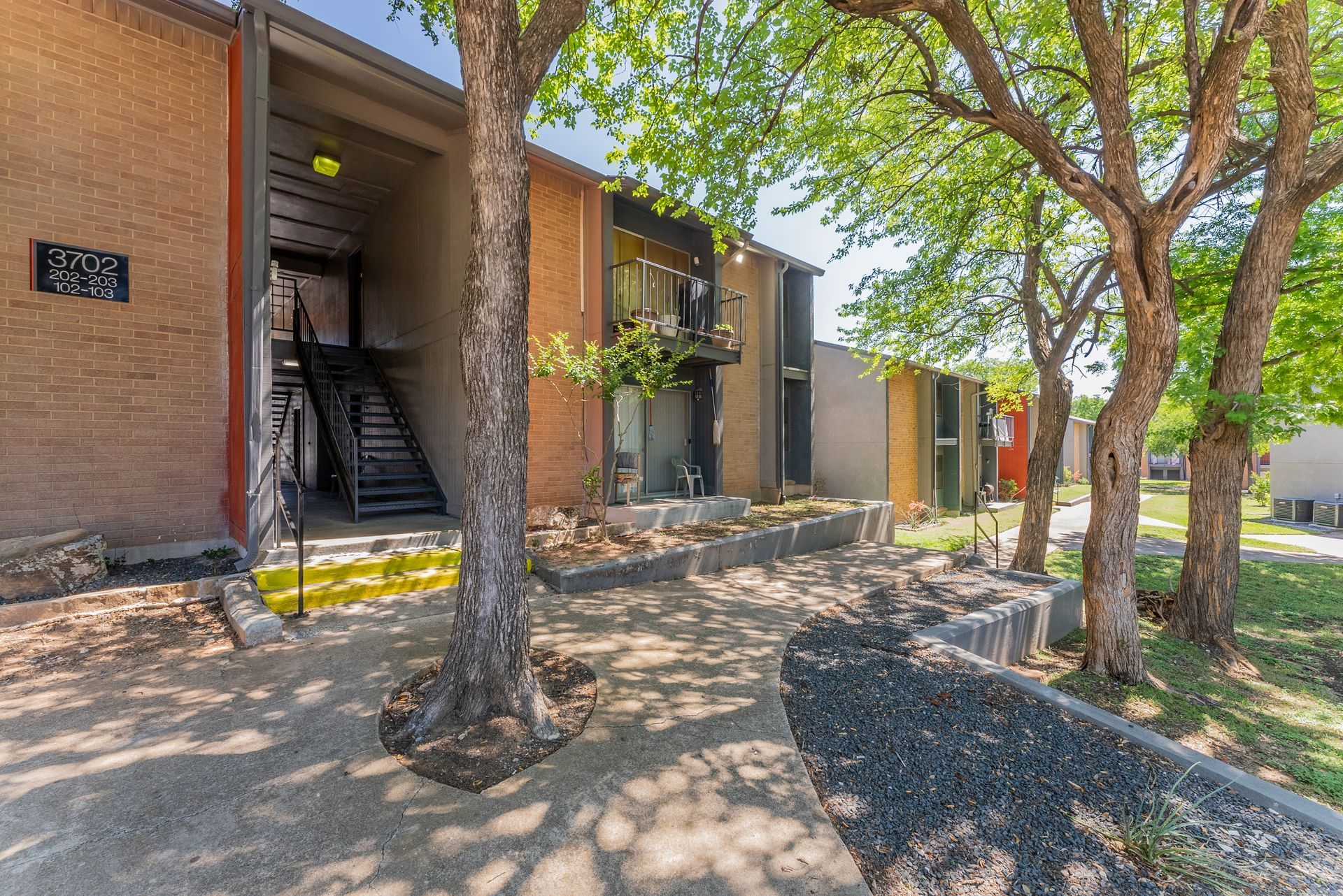 A brick apartment building with stairs and trees in front of it.