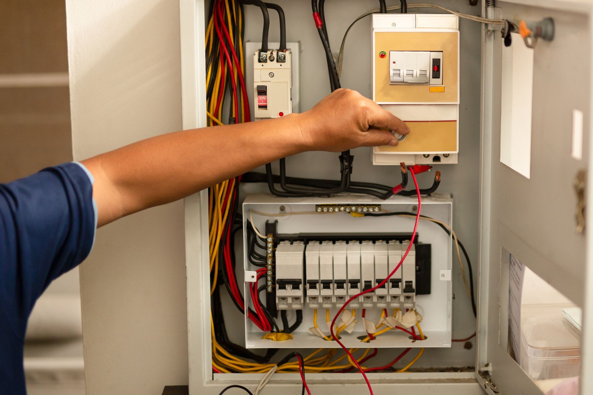 Technician pointing at electrical control panel with wires and breakers inside a cabinet