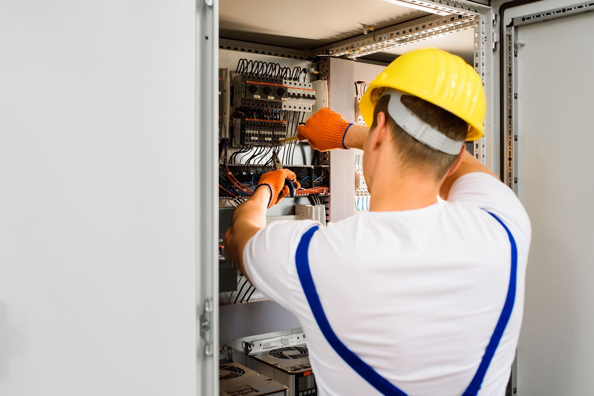 Electrician in hard hat working inside an open electrical control panel
