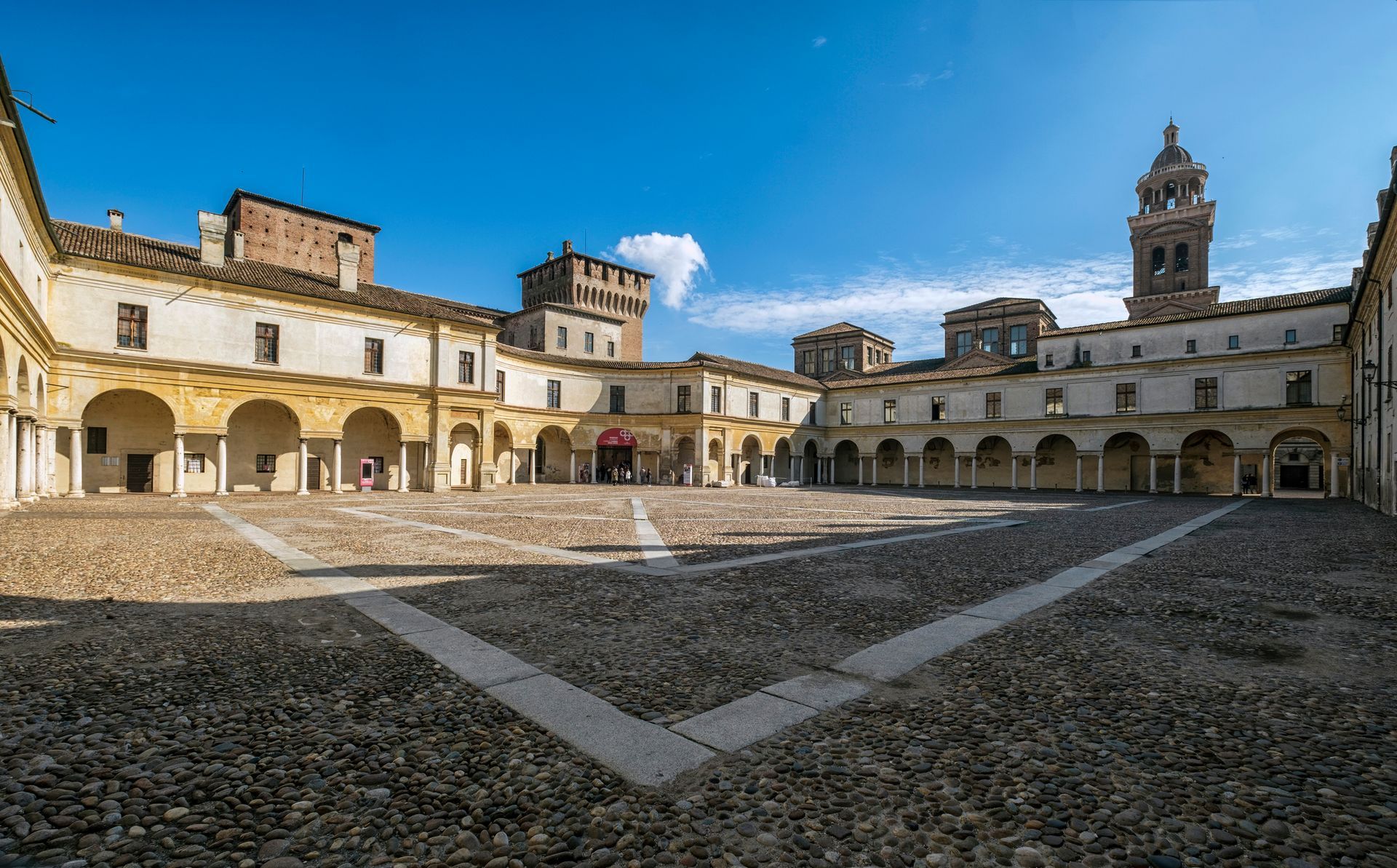 Un grande edificio con archi e una torre dell'orologio al centro di un cortile.
