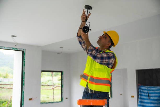 Construction worker on ladder installing ceiling light fixture during interior building project.