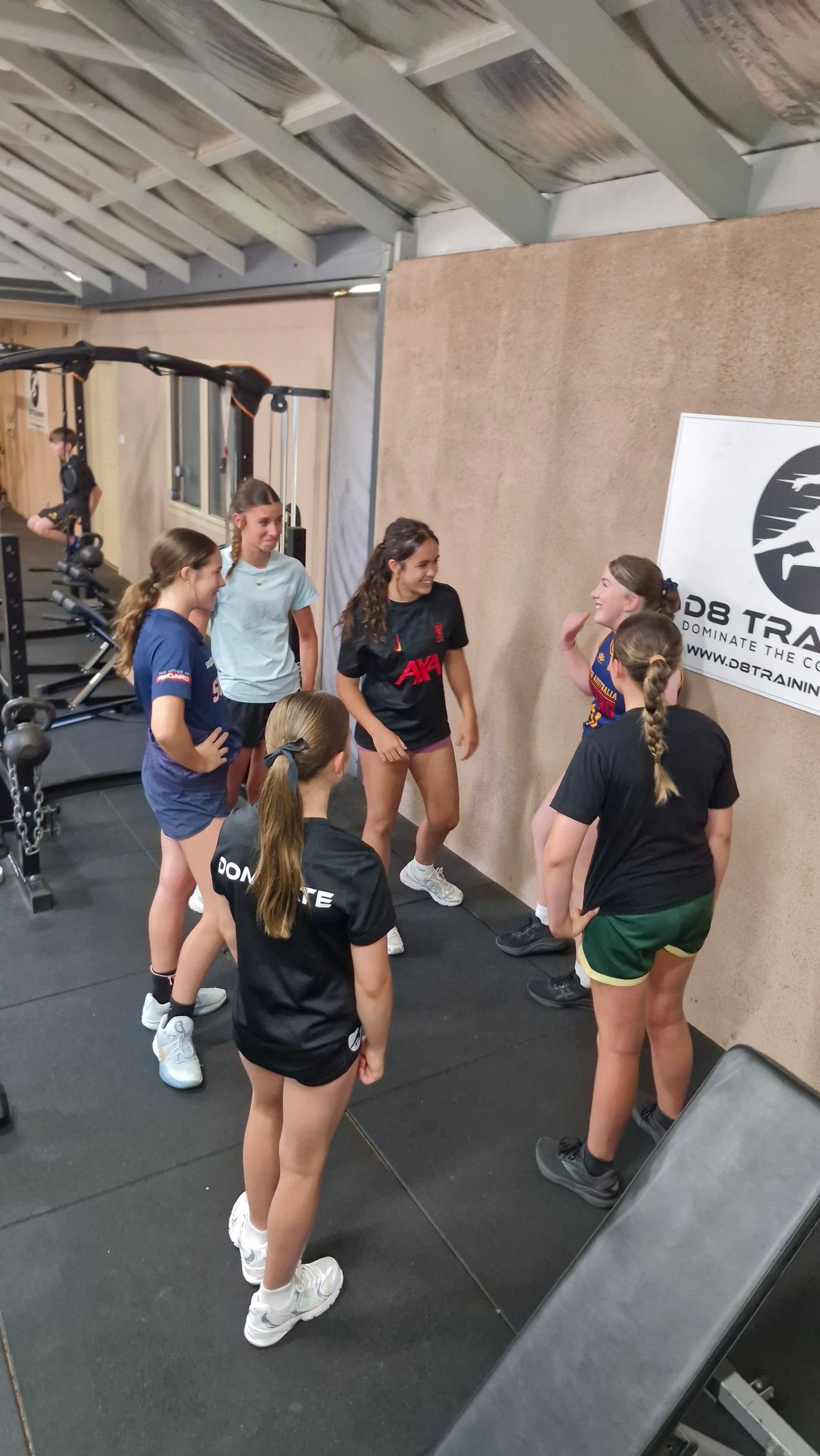 Group of young athletes in a gym, talking. Some wear athletic gear.