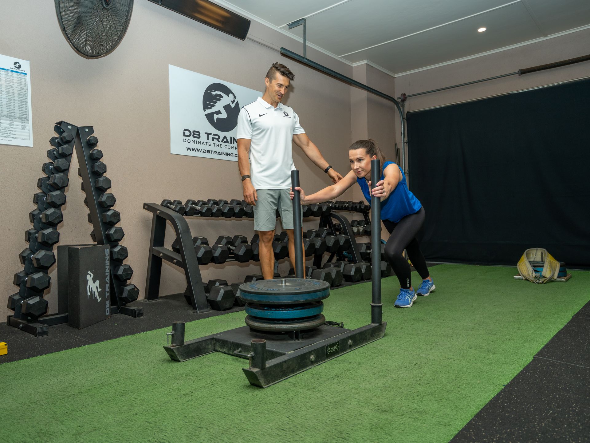 A man is helping a woman push a sled in a gym.