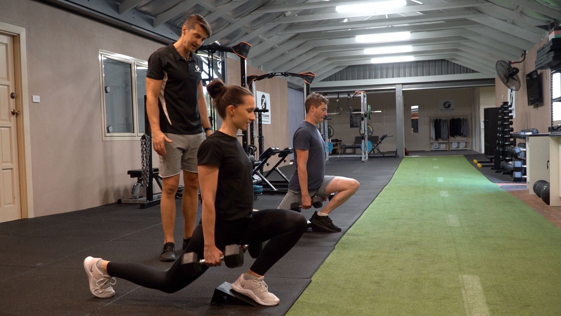 A man and a woman are doing lunges with dumbbells in a gym.
