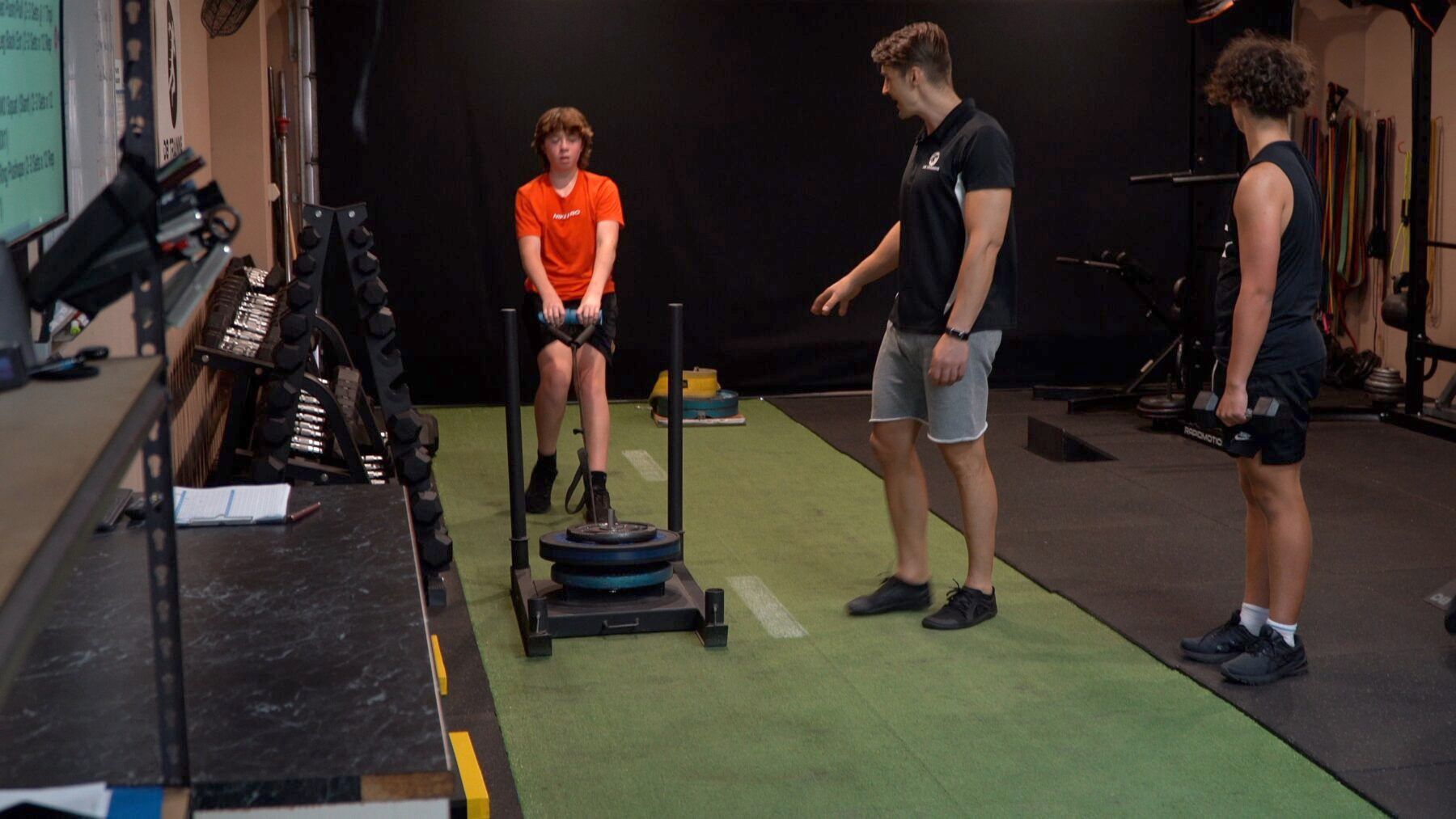 A group of people are standing around a sled in a gym.