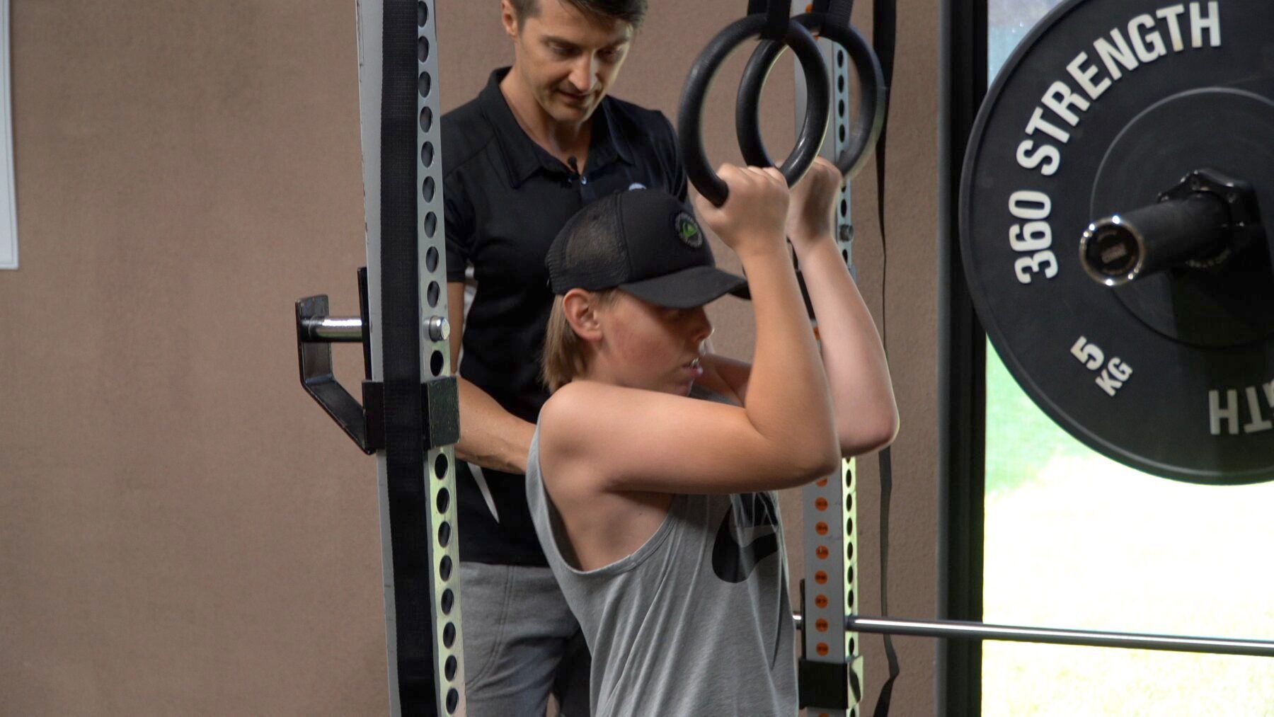 A man is helping a young boy lift rings in a gym.