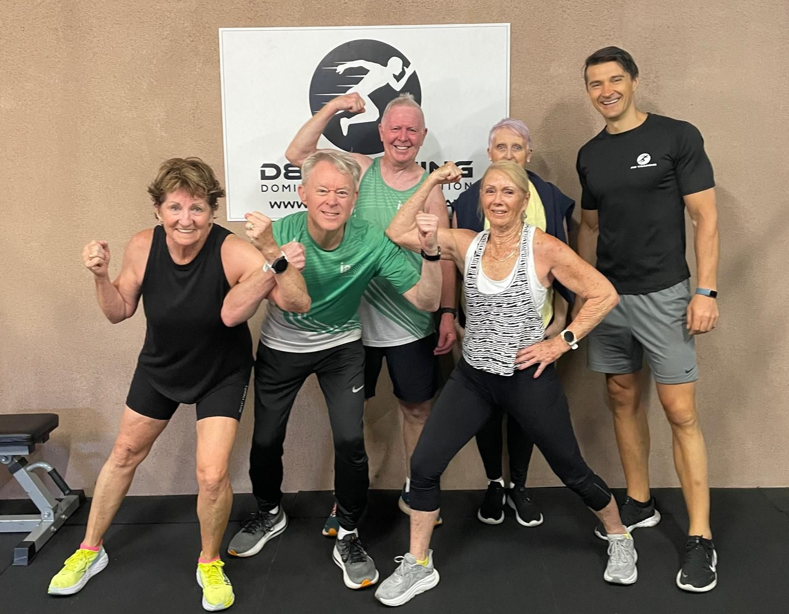 Group of people flexing, posing at a gym with instructor.