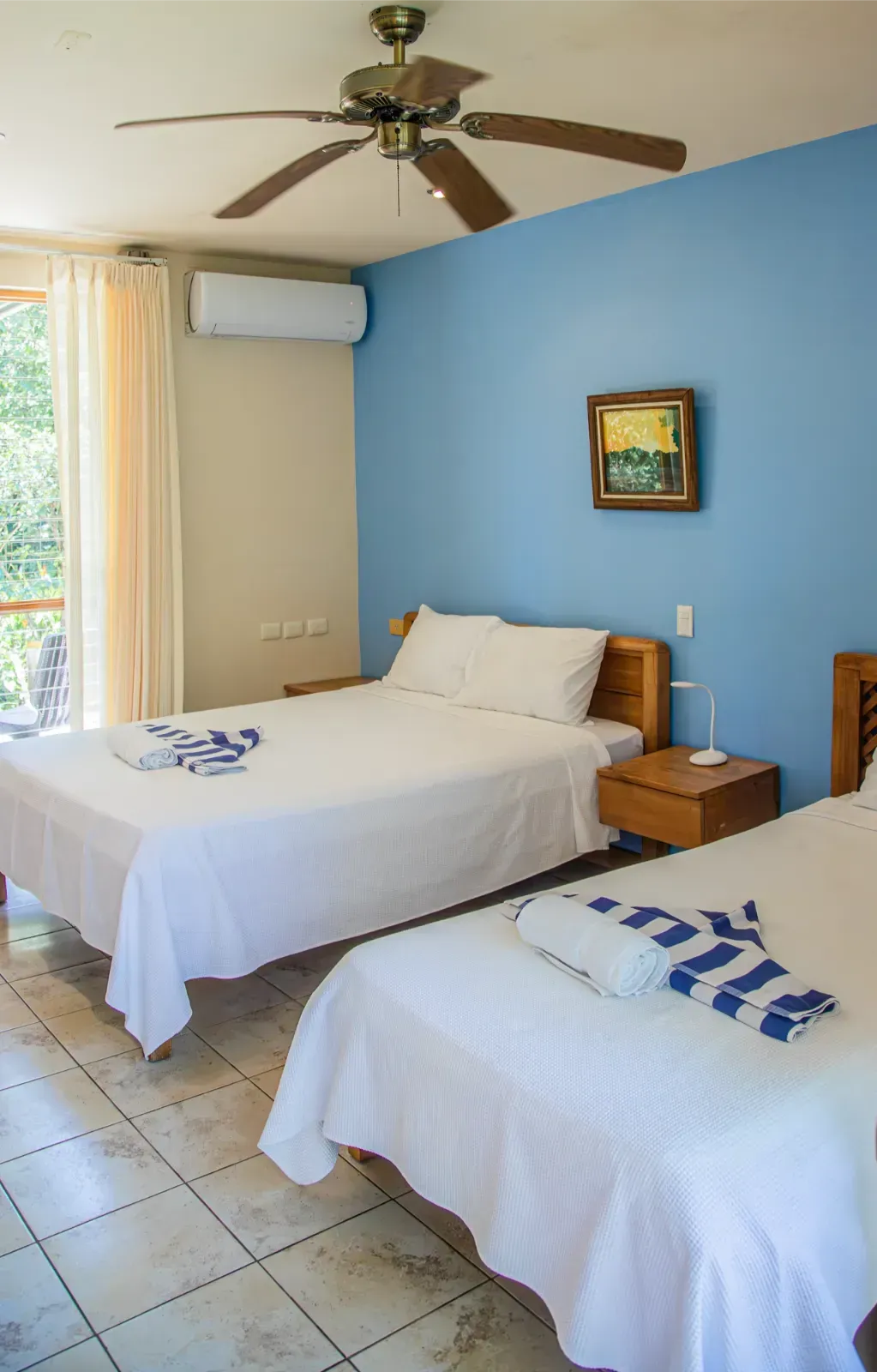 Bedroom with two beds, blue walls, wooden furniture, and ceiling fan.