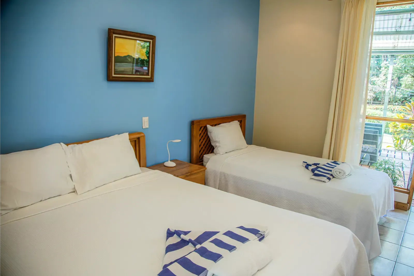 Bedroom with two beds, blue wall, art, and a view of trees.