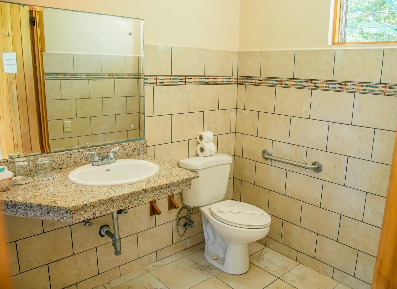 Bathroom with beige tile walls, white toilet, granite countertop, and accessible grab bar.
