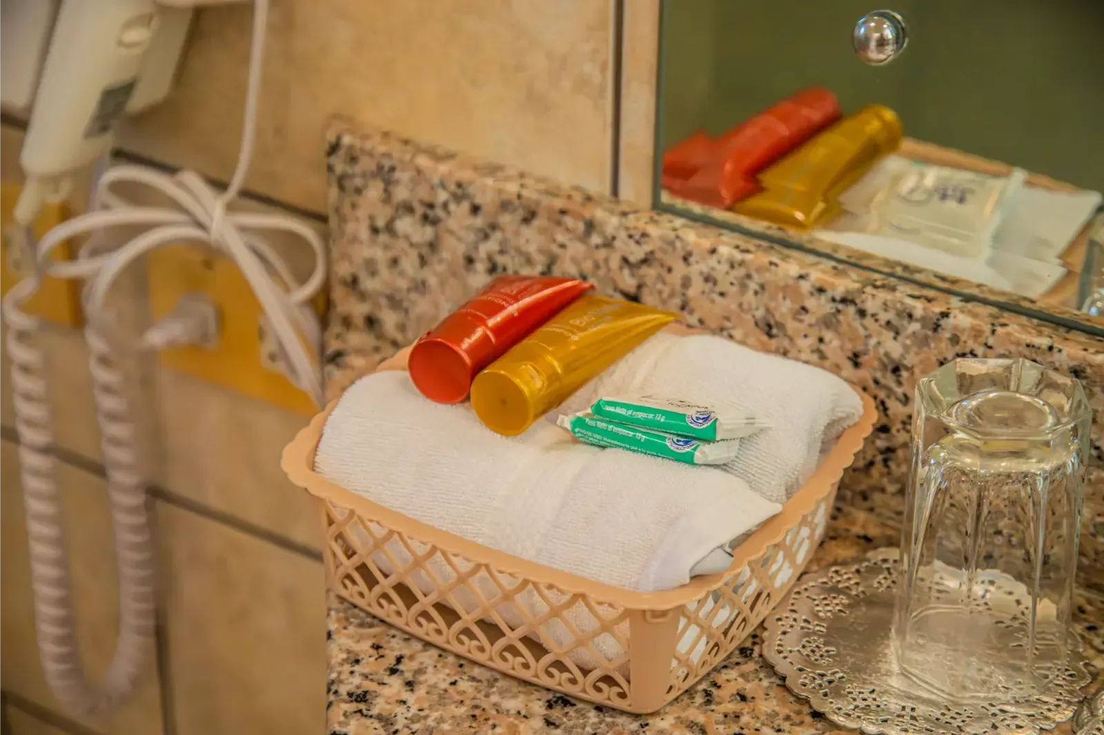 A bathroom countertop with a basket of towels, toiletries, and a glass next to a mirror.