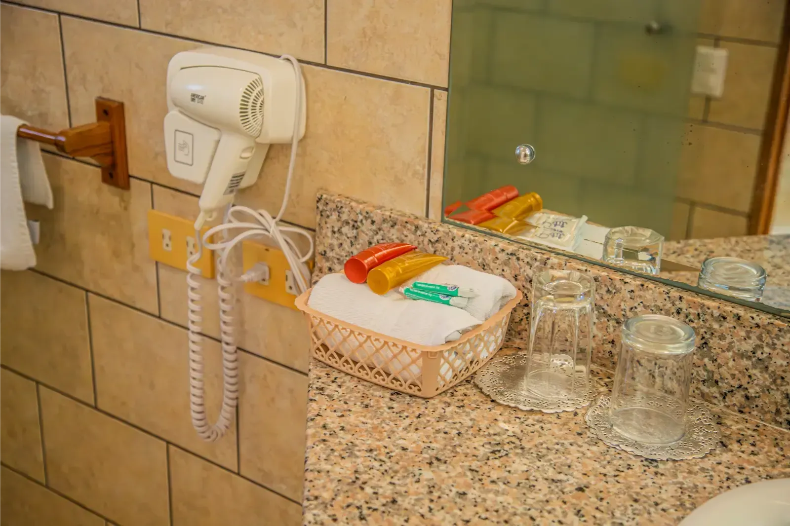 Bathroom counter with a hair dryer, toiletries, and glasses.