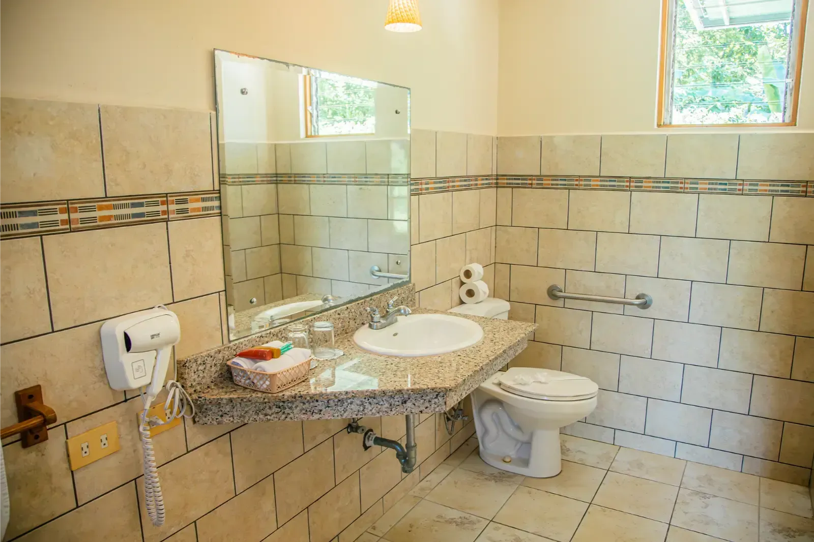 Bathroom with beige tile, a marble-look countertop, and a toilet. A mirror and a window are visible.