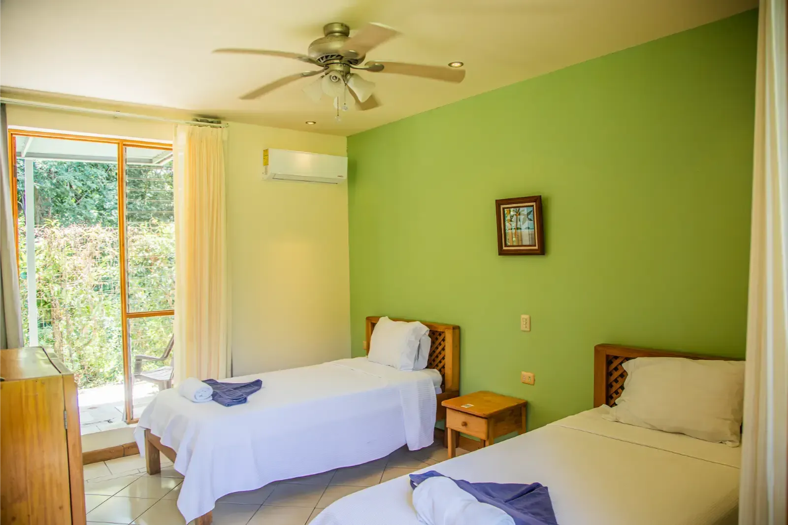 Two twin beds in a room with green walls, a ceiling fan, and a sliding glass door to a garden.