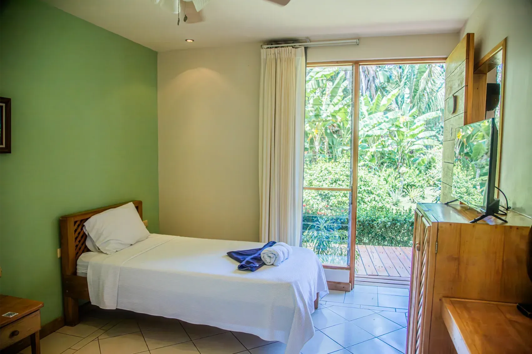 Bedroom with single bed, green wall, and sliding door to outdoor greenery.