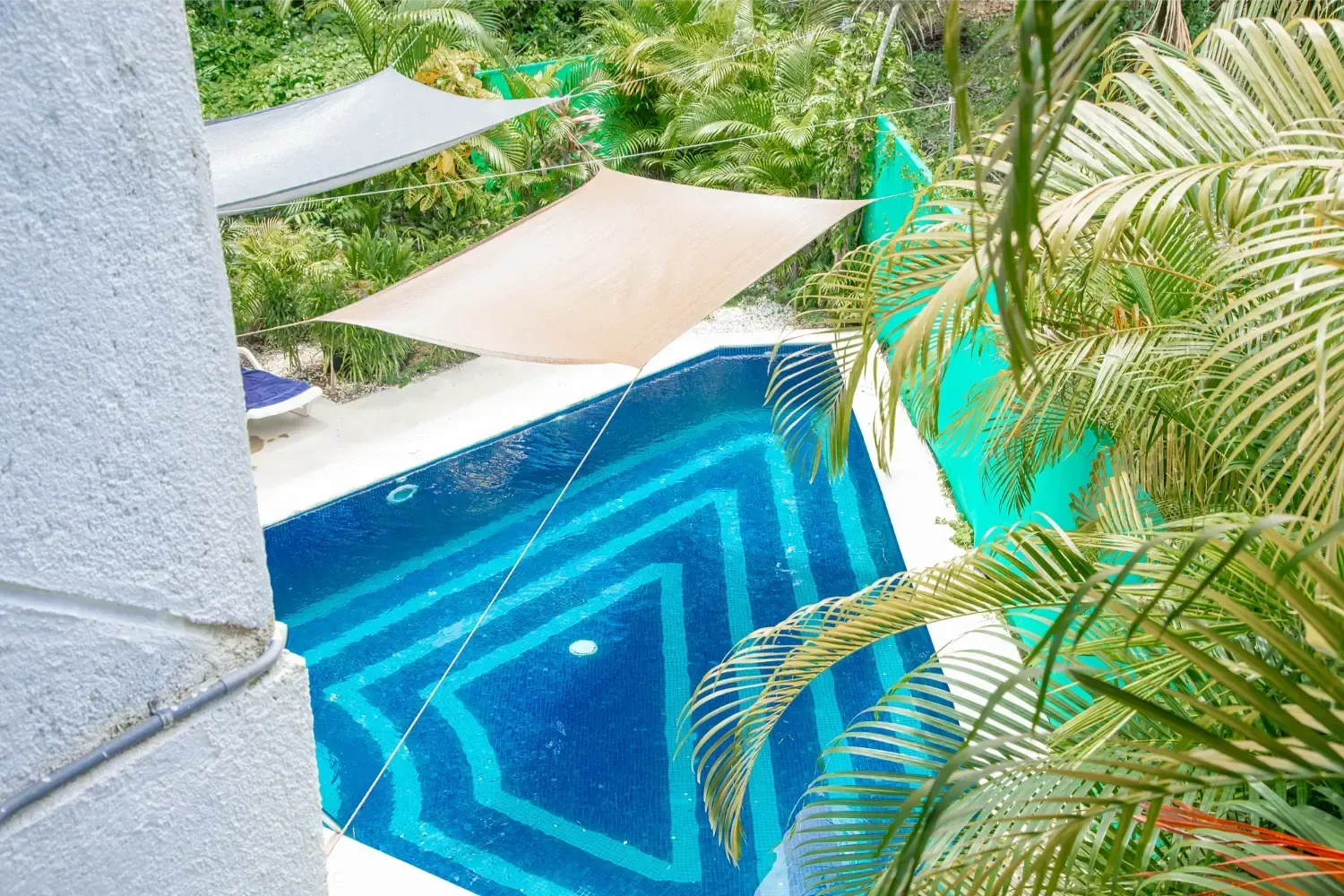 Pool with blue geometric tile, shaded by canvas canopies, surrounded by lush greenery.