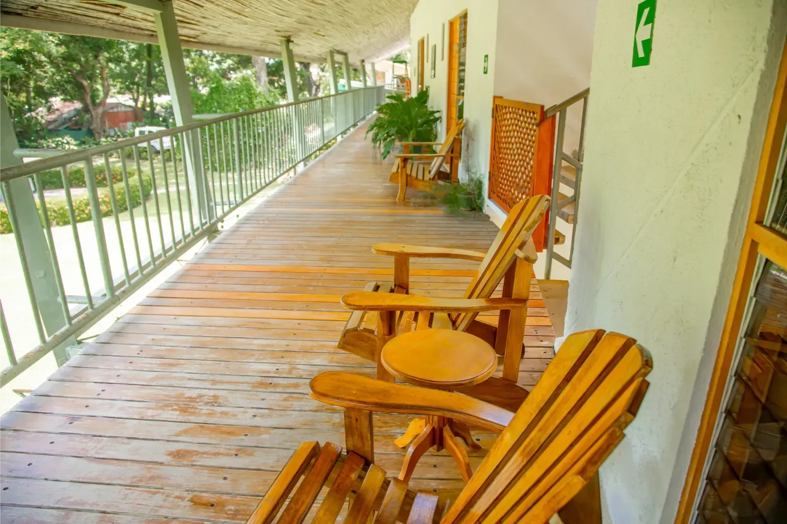 Wooden chairs on a long wooden balcony with metal railing, looking out on a green landscape.