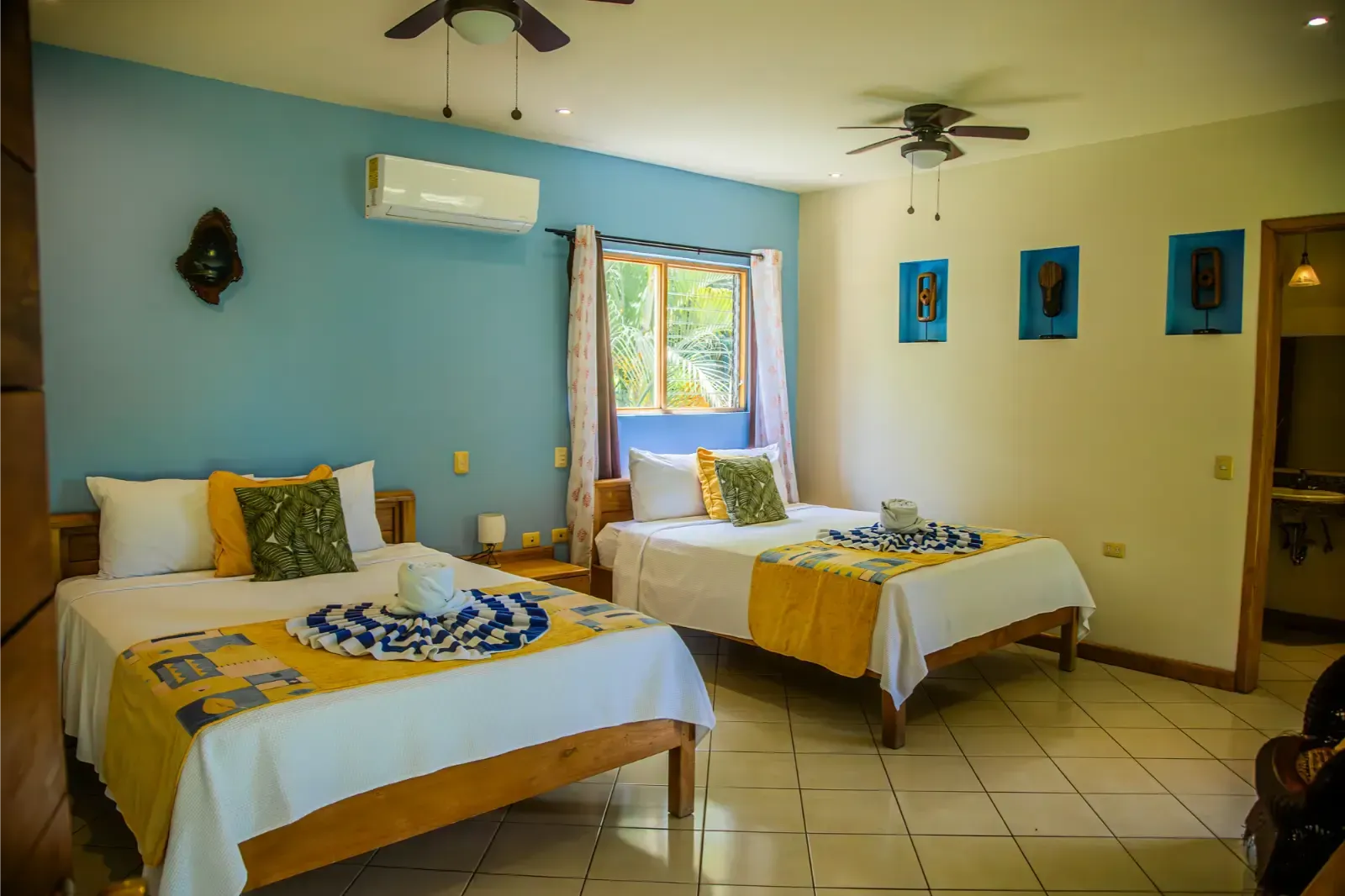 Two beds in a room with blue and yellow accents, a window, and ceiling fans.