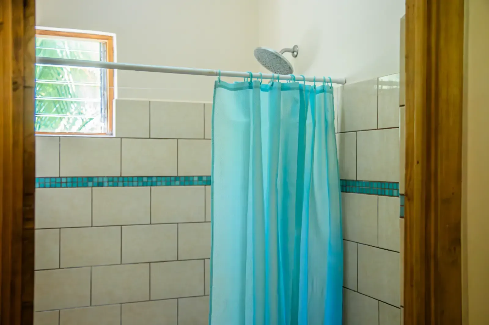 Shower with blue curtain, white tile, small window. Wooden door frames.