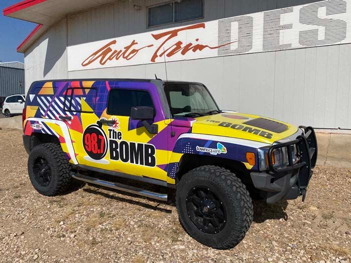 A customized yellow, purple, and blue Hummer with black wheels parked in front of an auto shop.