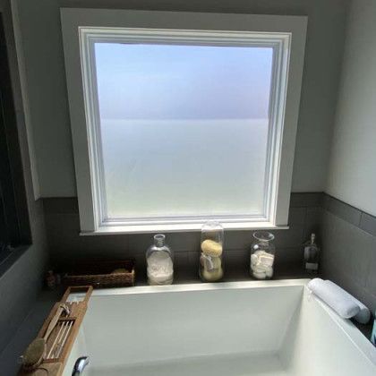 Bathroom with a frosted window above a white bathtub with toiletries on a ledge.