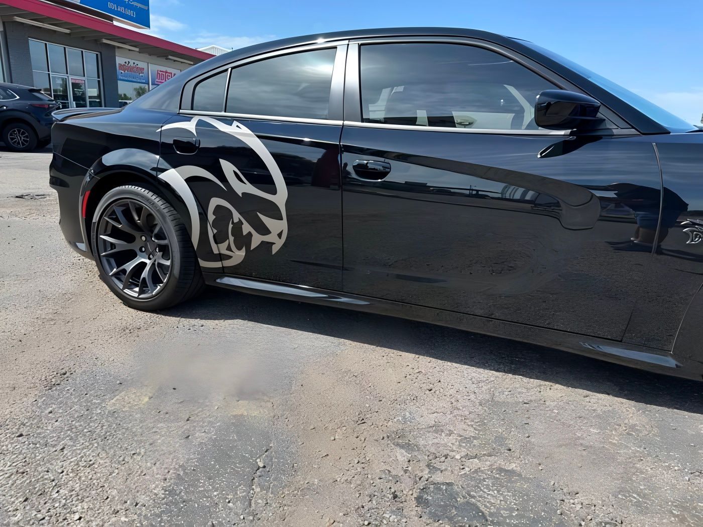Black Dodge Charger with silver Hellcat logo, parked on asphalt.