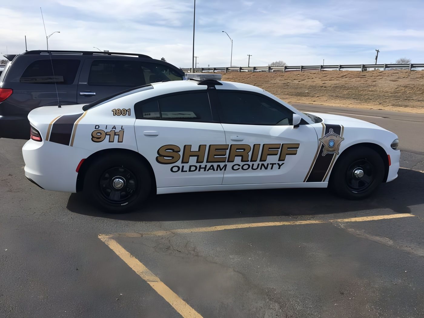 White Oldham County Sheriff's car parked in a parking lot. Black and tan details, dark tinted windows, and 911 markings.