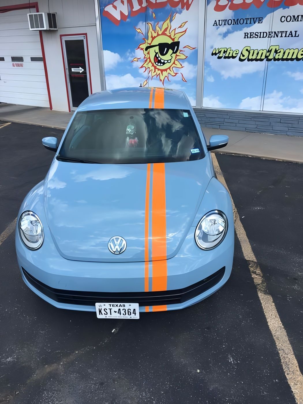 Blue VW Beetle with orange racing stripes parked in front of a building with a 