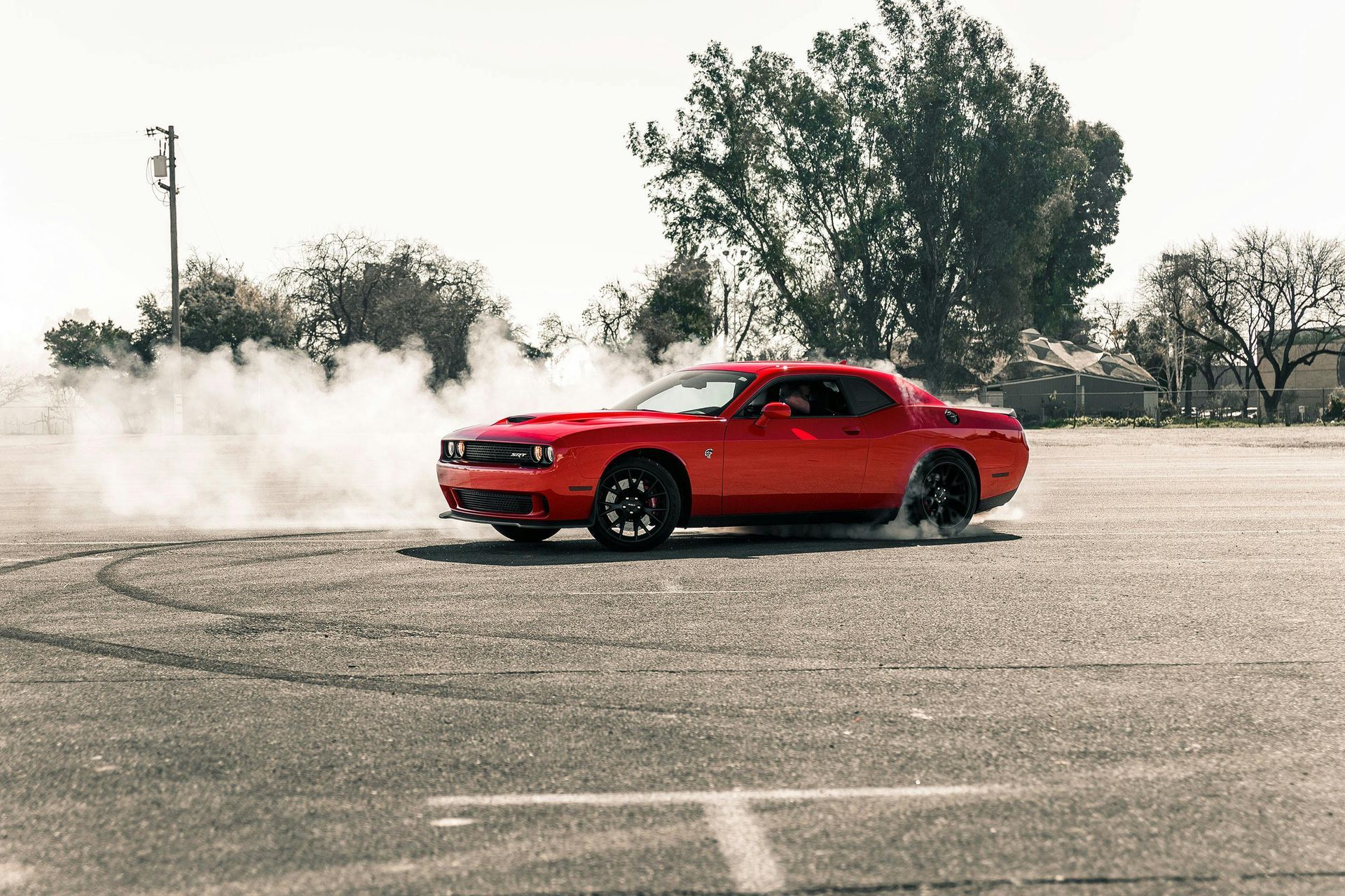 Red Dodge Challenger car performing a burnout, producing tire smoke on a paved area.