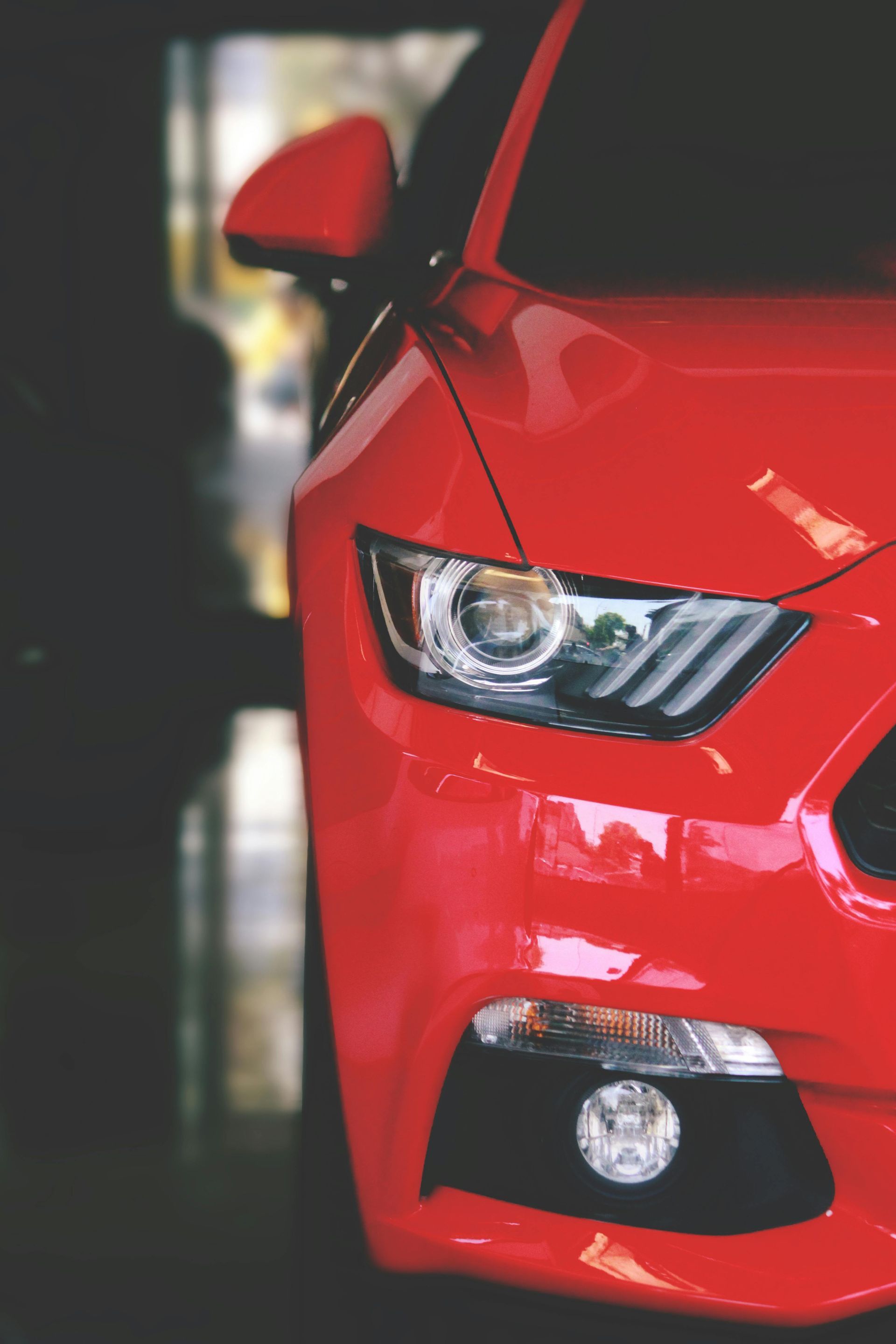 Red Ford Mustang's front end, parked indoors, with headlights and side mirror visible.