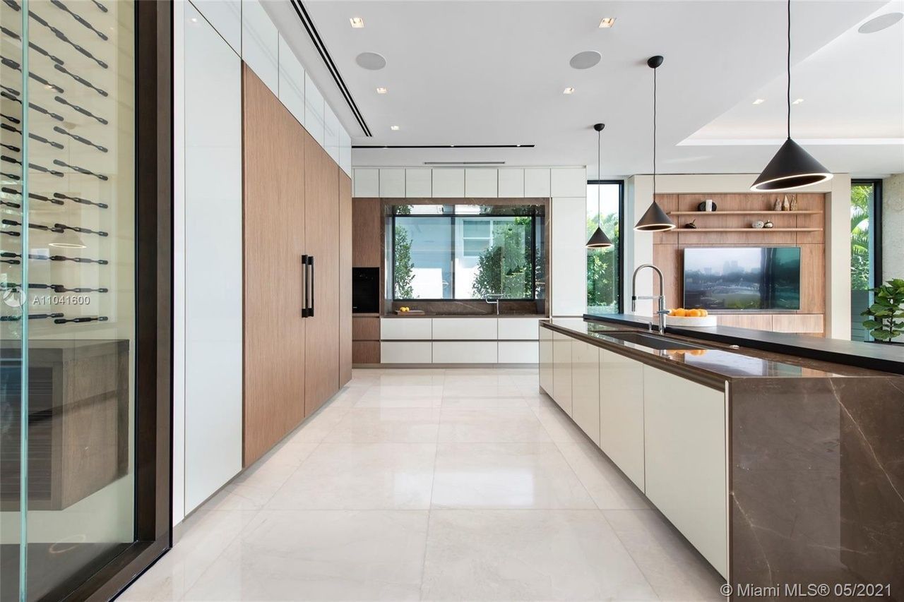 Modern kitchen with wooden cabinetry, marble countertops, and large island with pendant lights.