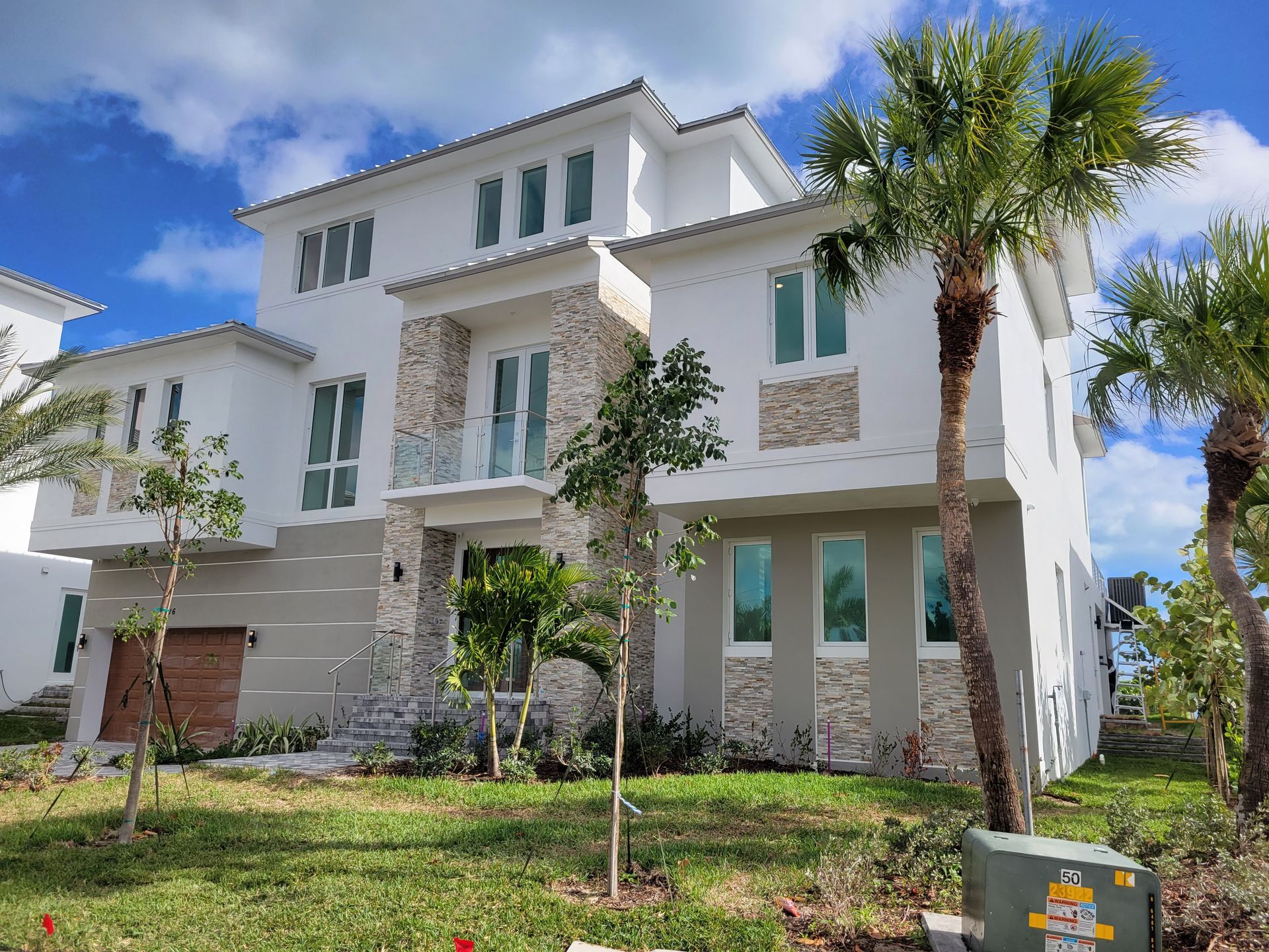 White multi-story house with stone accents, palm trees, and blue sky.