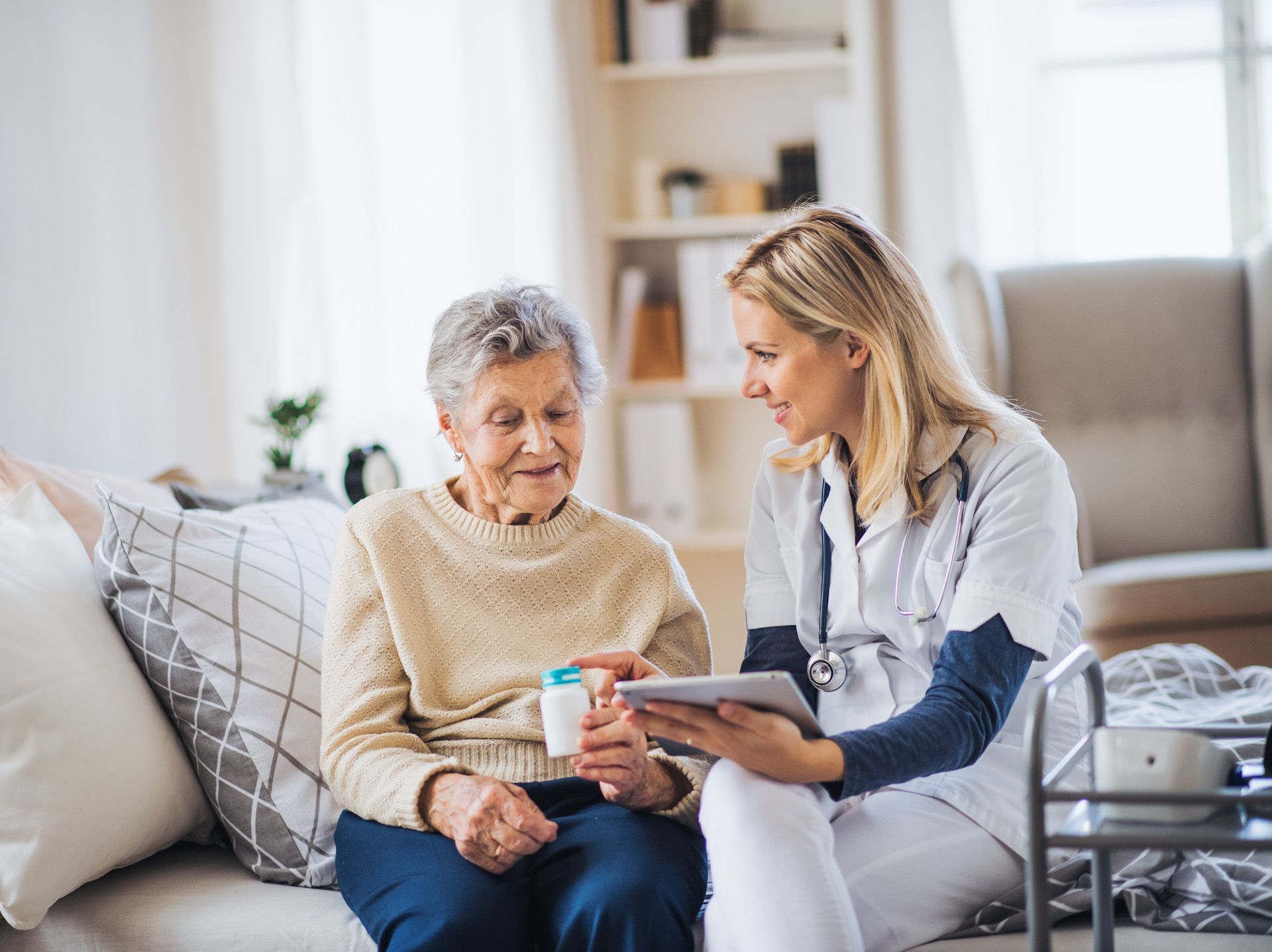 A nurse is talking to an elderly woman while sitting on a couch.
