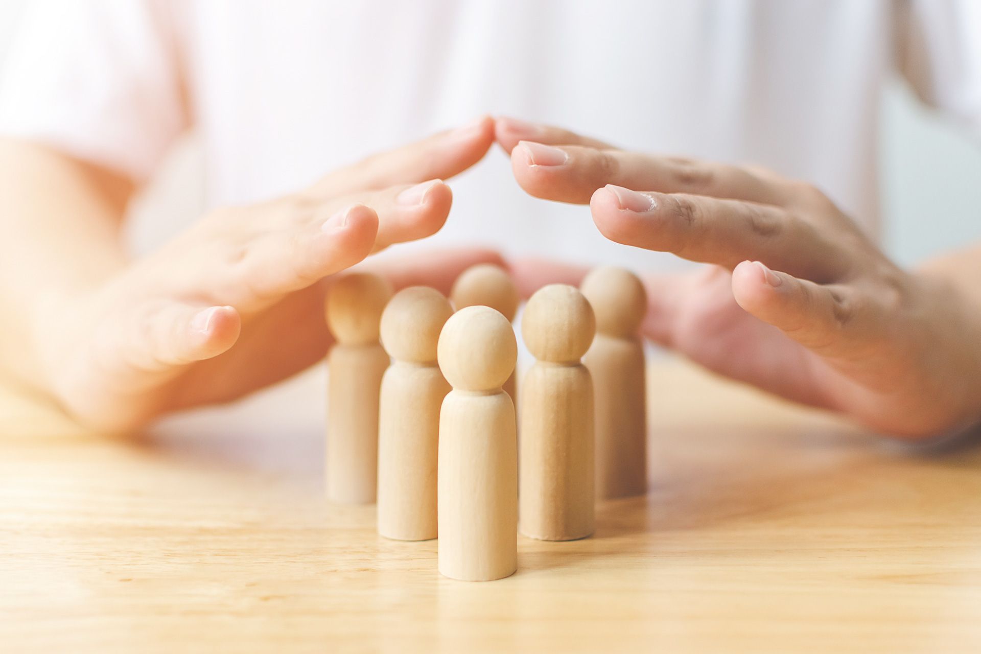 A person is covering a group of wooden people with their hands.