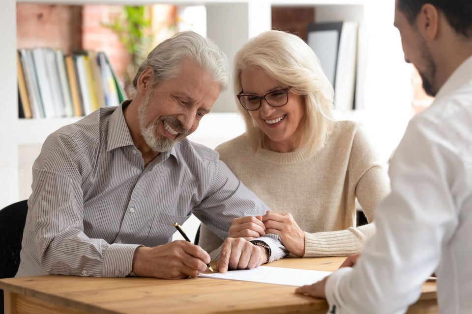 An elderly couple is signing a document with a man.