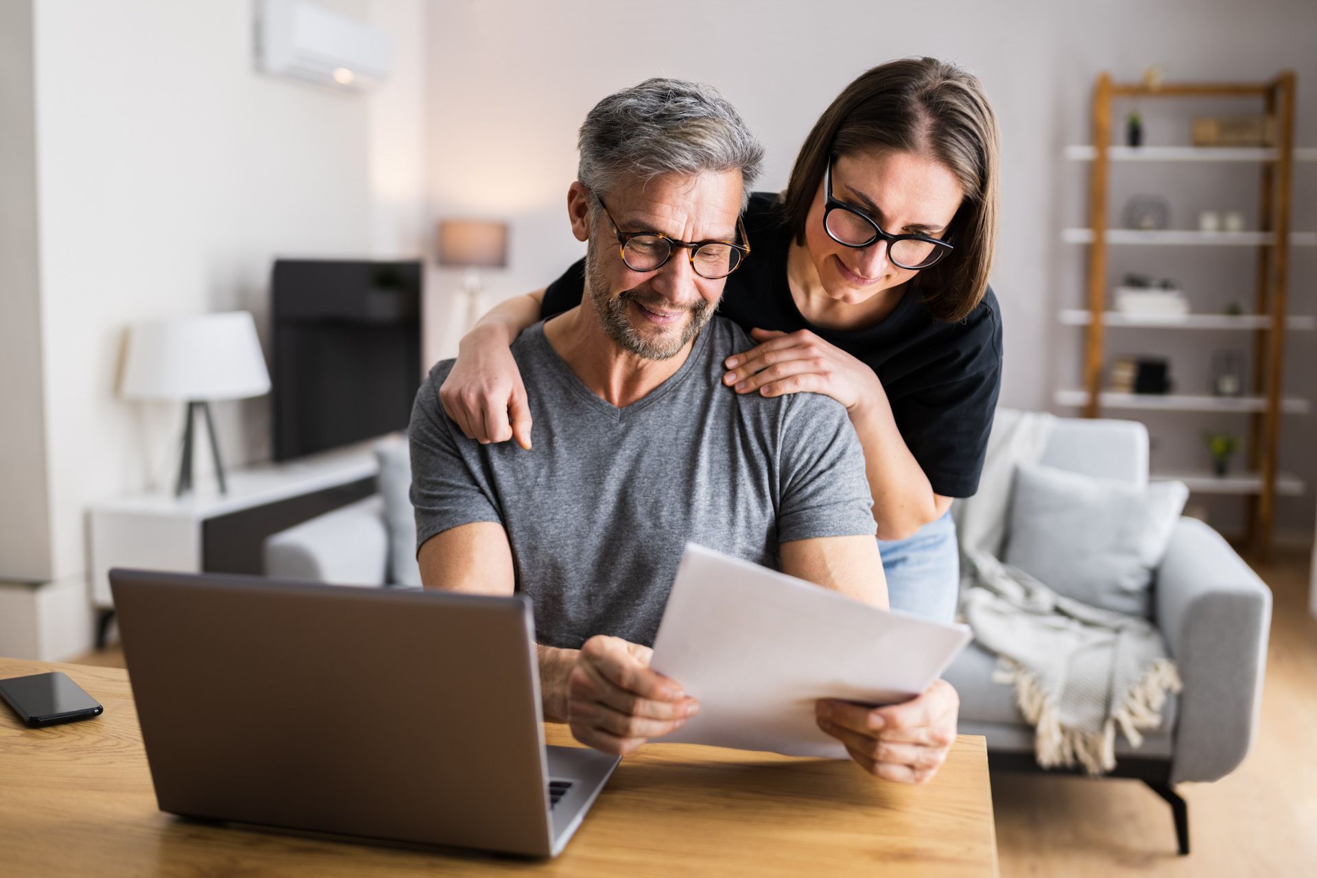 A man and a woman are sitting at a table looking at a laptop.