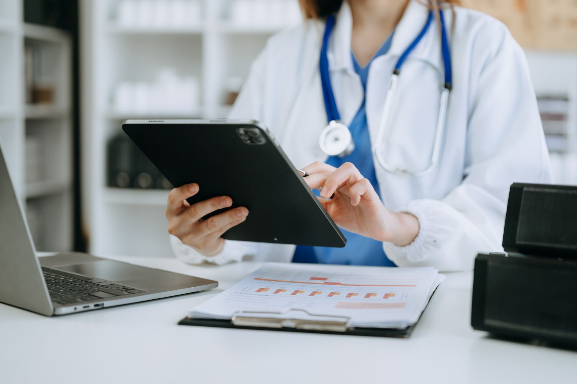 A doctor is sitting at a desk using a tablet computer.
