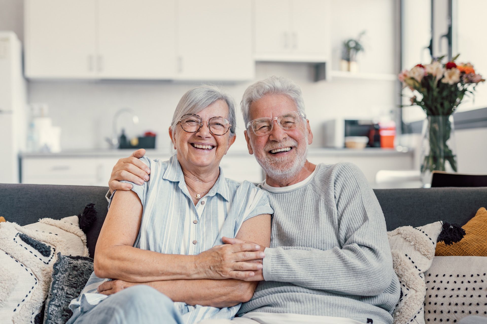 An elderly couple is sitting on a couch and smiling for the camera.