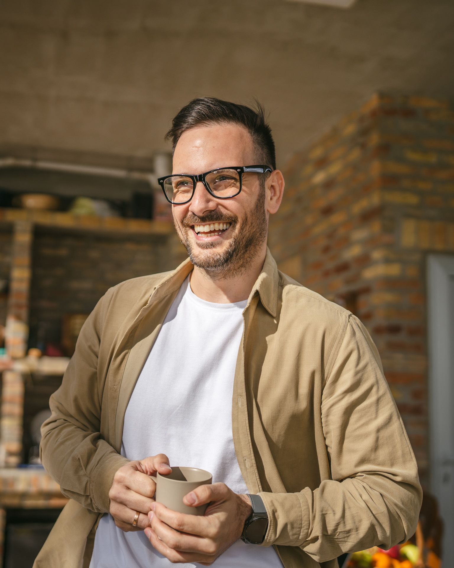 A man wearing glasses is holding a cup of coffee and smiling.