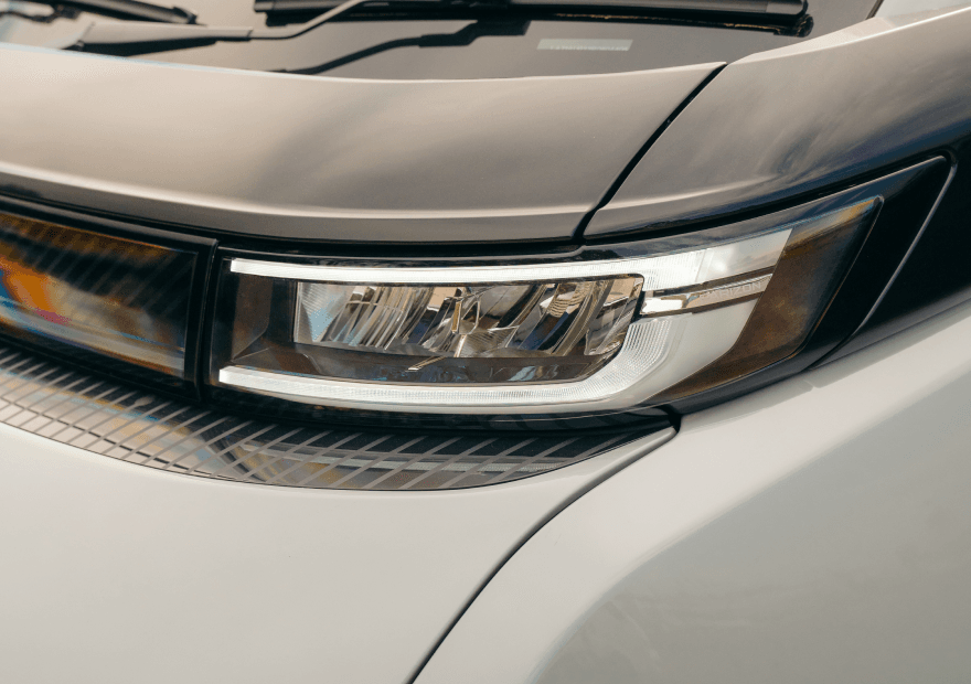 A close-up of a modern vehicle's headlight assembly with a silver metallic accent and a white body panel.