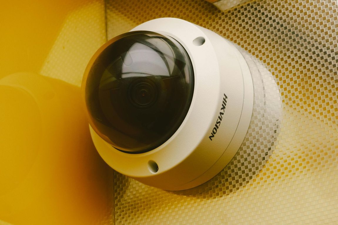 Two security cameras mounted on a pole under a lit metal roof, tinted purple and green