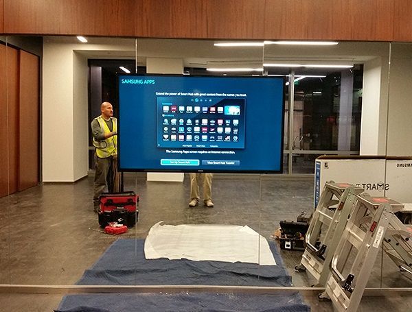 Airport hallway with workers setting up a large digital display and equipment on the floor