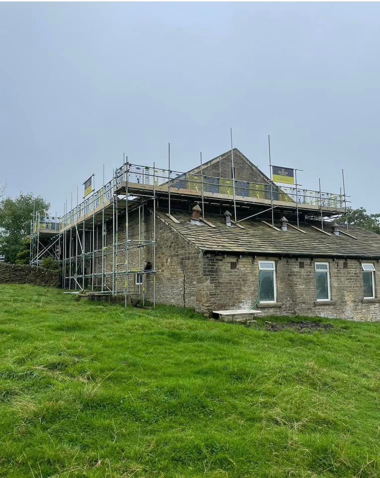 A large stone building with scaffolding on the roof is being built in a grassy field.