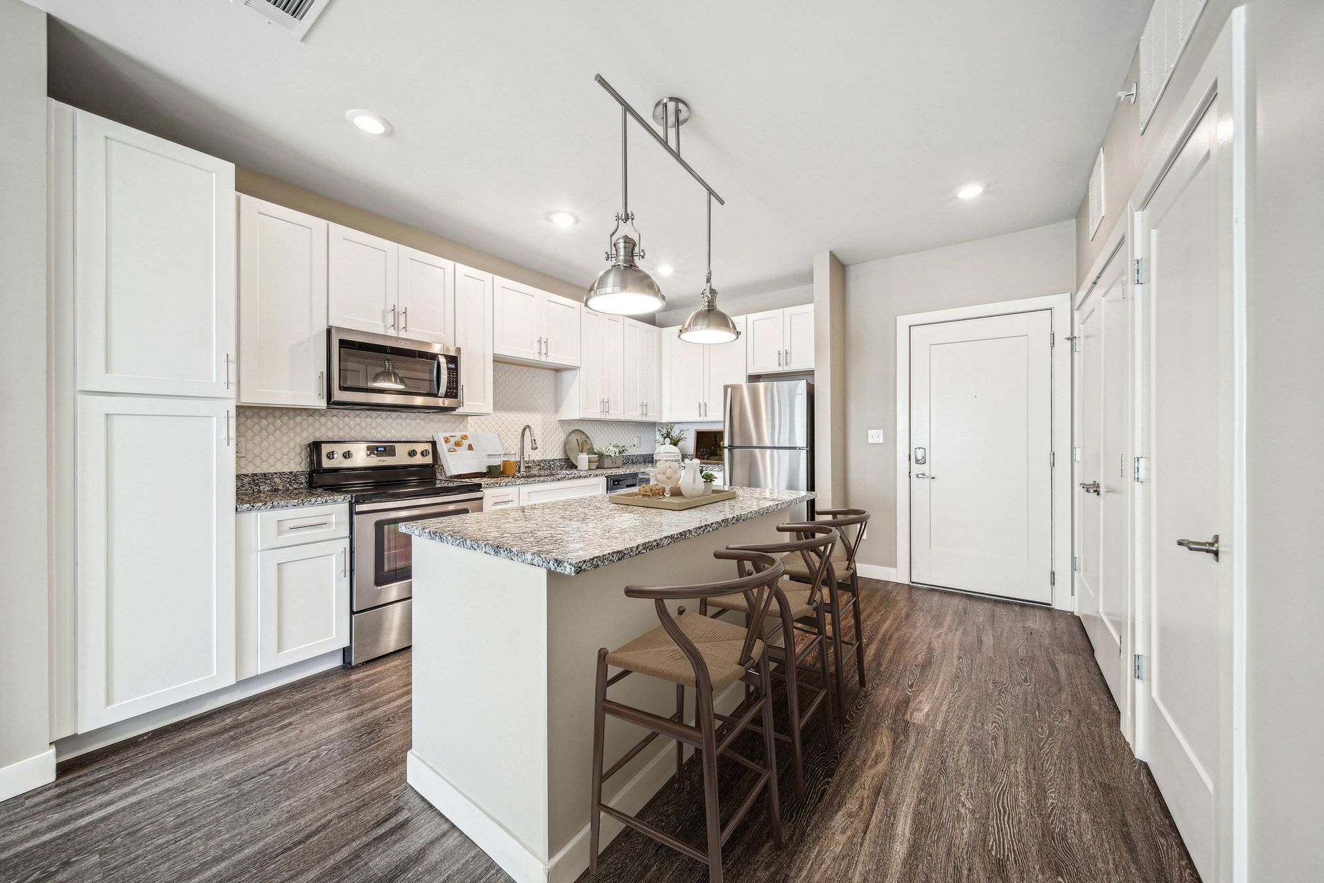 Modern white kitchen with granite countertops, island seating, and stainless steel appliances.